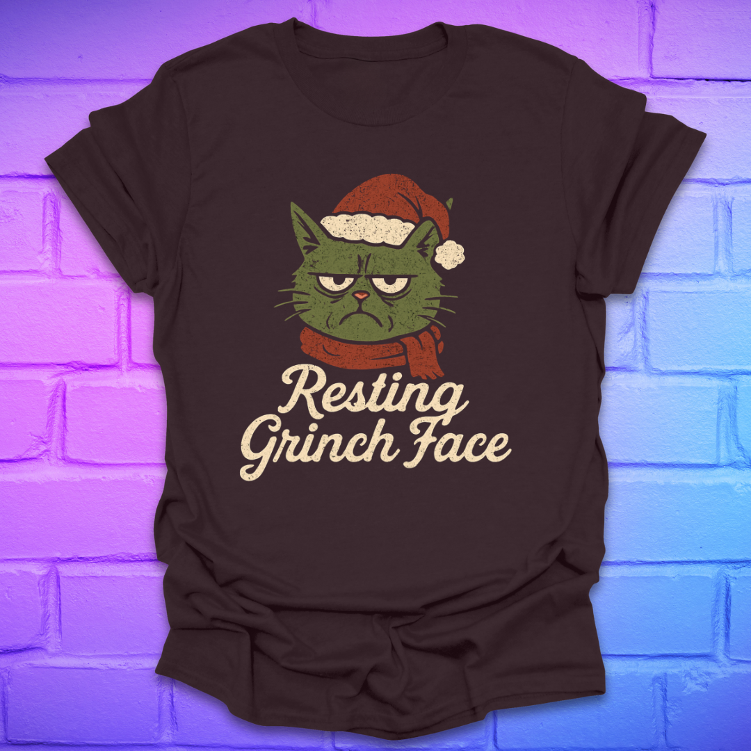 Brown t-shirt with a cartoon cat wearing a Santa hat and scarf, text 'Resting Grinch Face' on a brick wall background.