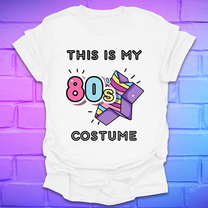 White t-shirt with 'This is my 80s costume' text and colorful design on a purple brick wall background