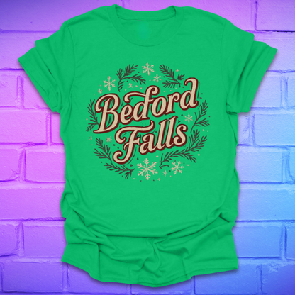 Green T-shirt with chrismas theme text, "Bedford Falls" surrounded by pine and snowflakes on a brick background.