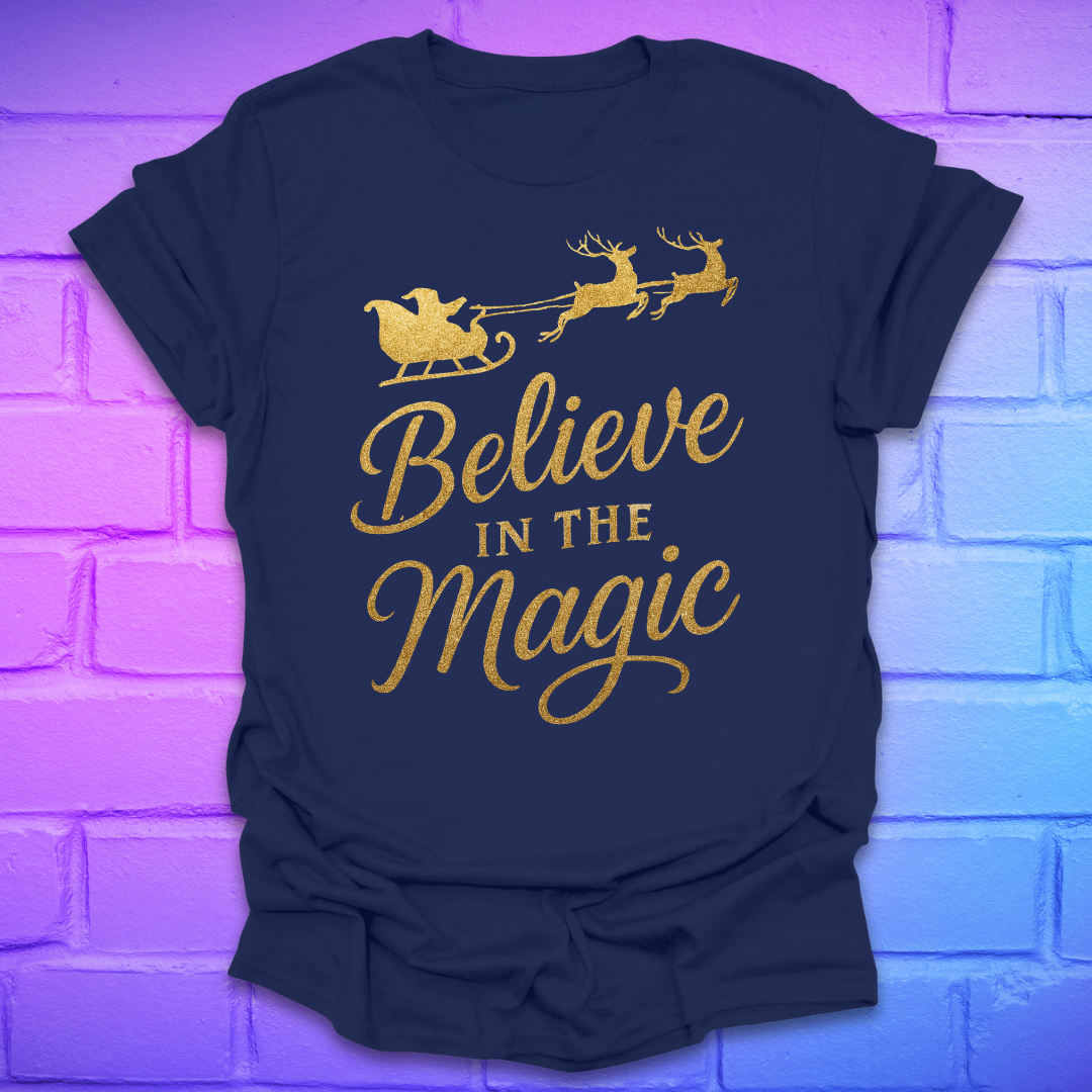 Navy blue t-shirt with gold 'Believe in the Magic' text and Santa sleigh design on a brick wall background.