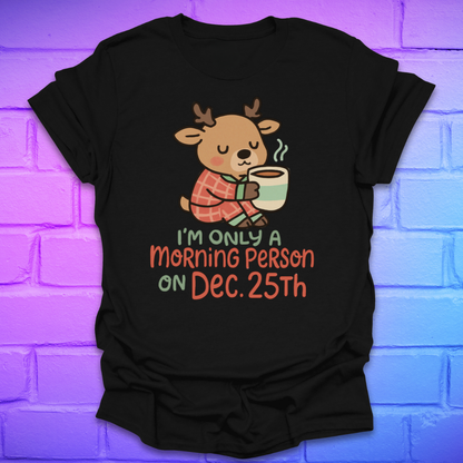 Black t-shirt with a cartoon deer holding a mug and text, 'only a morning person on Dec 25', on a brick wall background