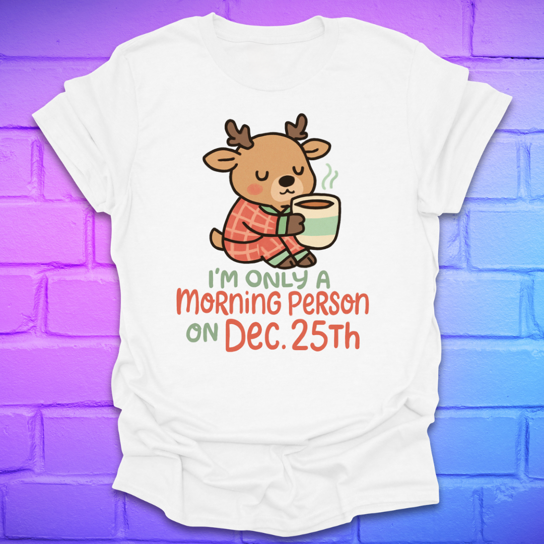 White t-shirt with a cartoon deer holding a mug and text, 'only a morning person on Dec 25', on a brick wall background