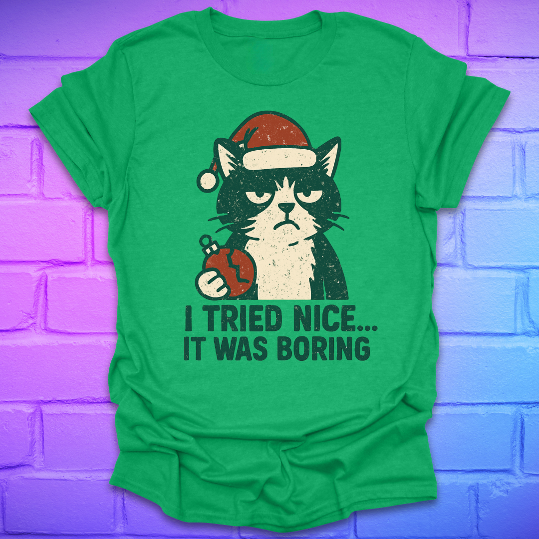 Irish green t-shirt with a frowning cat holding a broken christmas ball with text, 'i tried nice. it was boring'. on a brick background.