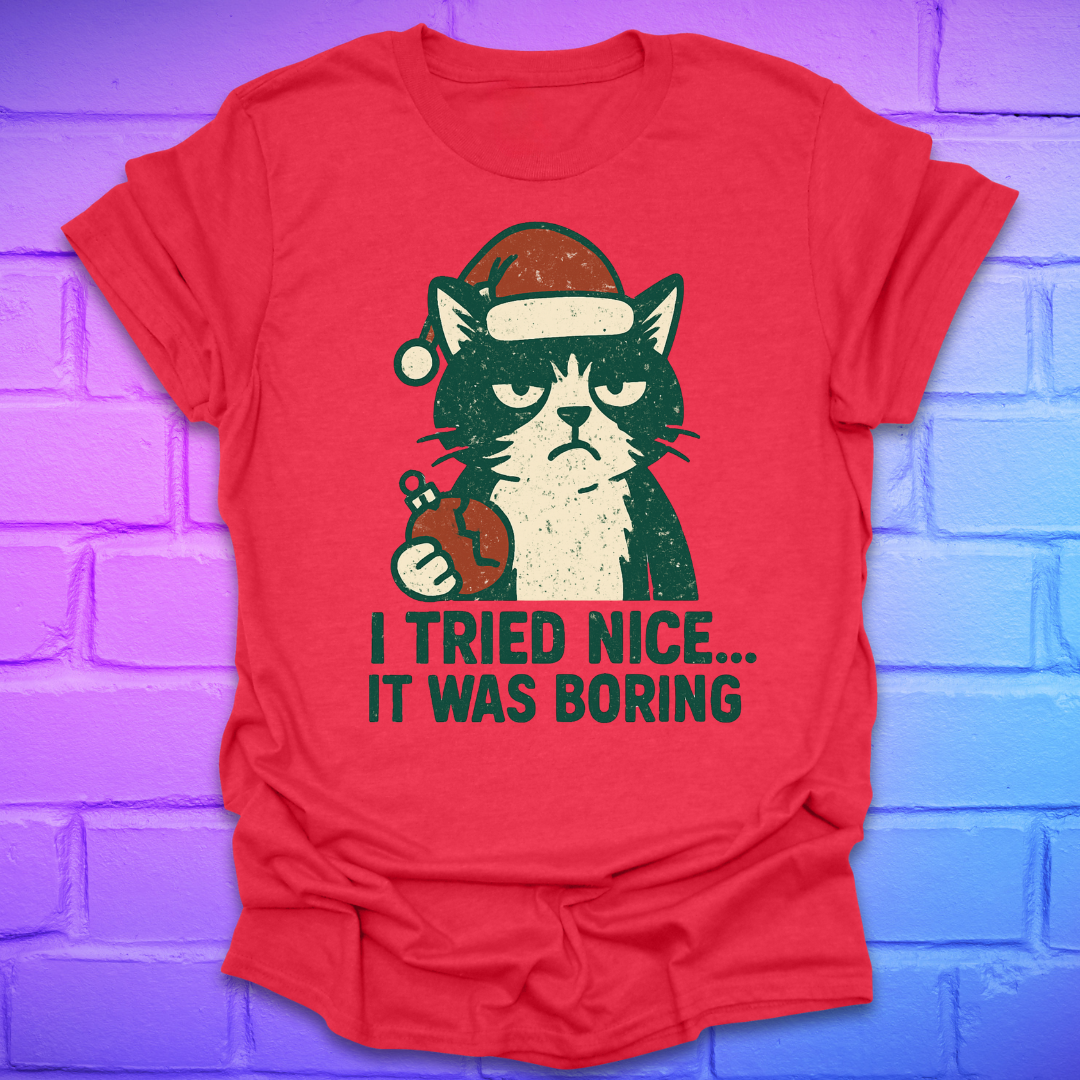 Red t-shirt with a frowning cat holding a broken christmas ball with text, 'i tried nice. it was boring'. on a brick background.