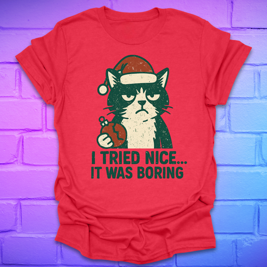 Red t-shirt with a frowning cat holding a broken christmas ball with text, 'i tried nice. it was boring'. on a brick background.