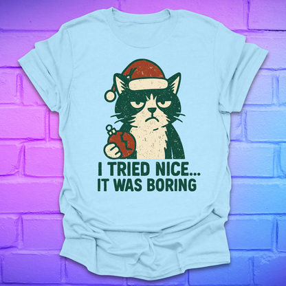 Light blue t-shirt with a frowning cat holding a broken christmas ball with text, 'i tried nice. it was boring'. on a brick background.