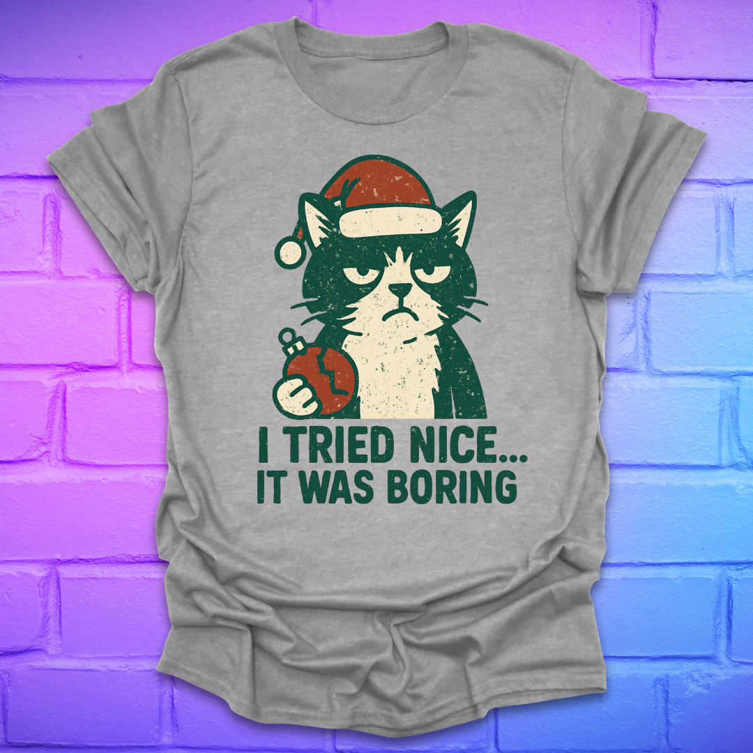 Grey t-shirt with a frowning cat holding a broken christmas ball with text, 'i tried nice. it was boring'. on a brick background.