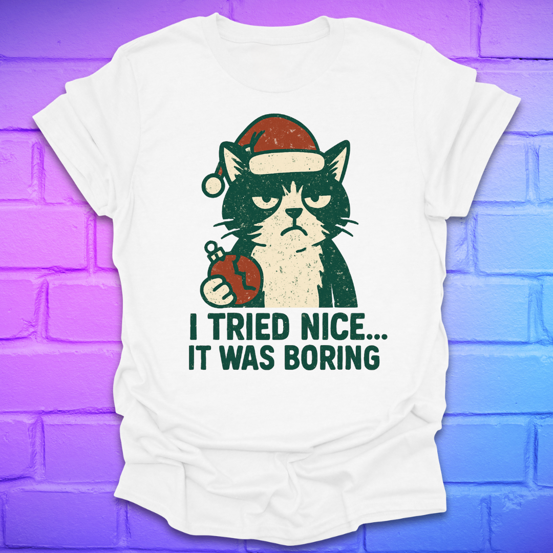 White t-shirt with a frowning cat holding a broken christmas ball with text, 'i tried nice. it was boring'. on a brick background.