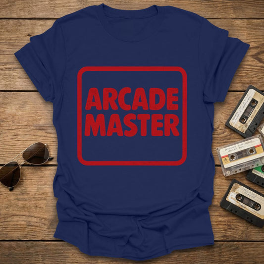 Blue t-shirt with 'Arcade Master' in red on a wooden surface with sunglasses and cassettes.