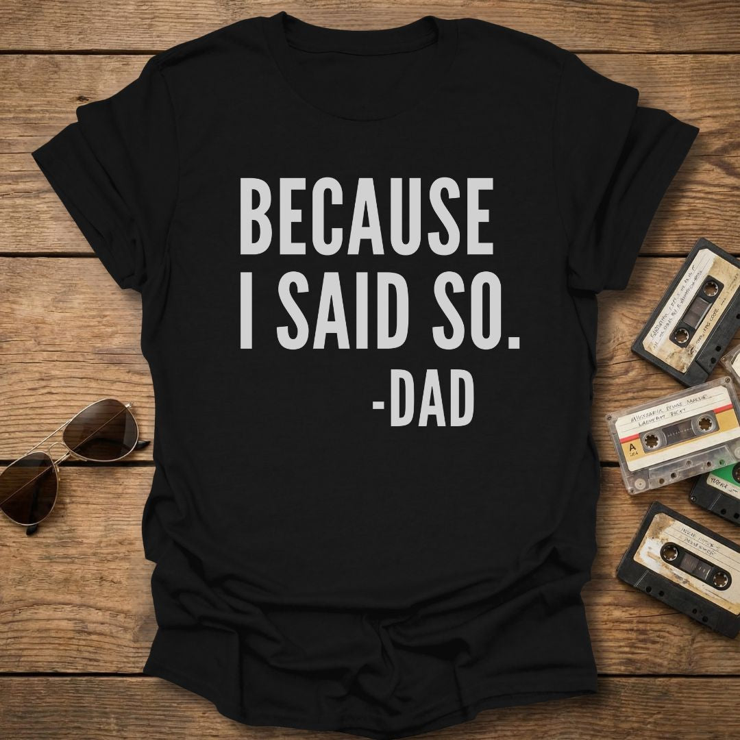 Black t-shirt with 'BECAUSE I SAID SO. -DAD' text on a wooden surface with sunglasses and cassettes.