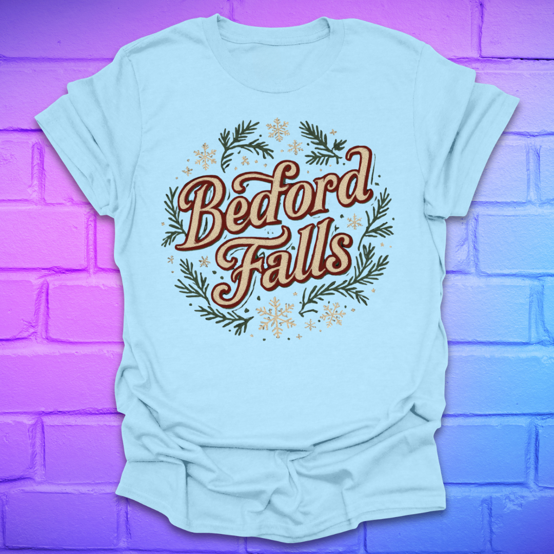 Light blue T-shirt with chrismas theme text, "Bedford Falls" surrounded by pine and snowflakes on a brick background.