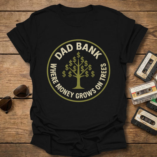 Black t-shirt with 'Dad Bank' graphic on a wooden surface with sunglasses and cassettes.