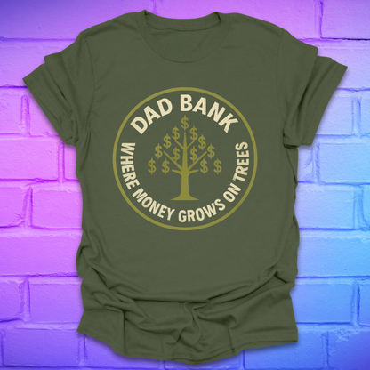 Green t-shirt with gold graphic and text 'Dad Bank. where money grows on trees' on a brick wall background