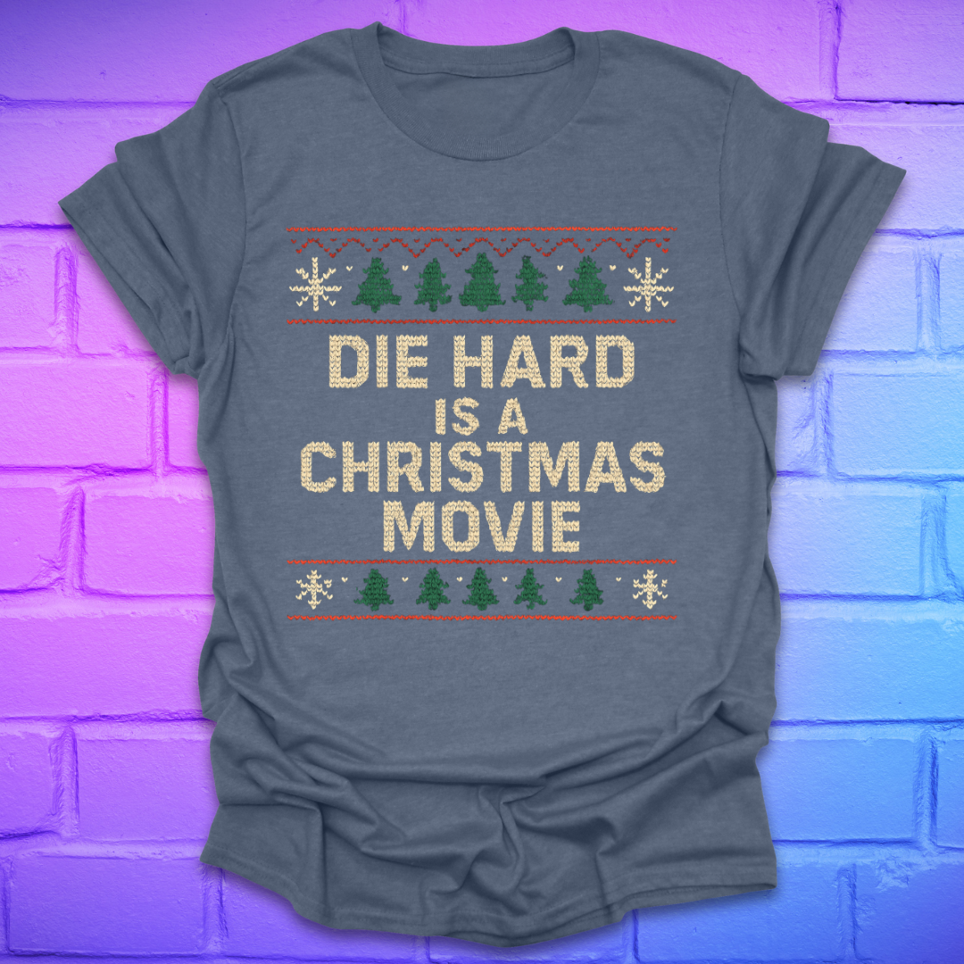 Gray t-shirt with 'Die Hard is a Christmas Movie' text and Christmas-themed graphics on a brick wall background.