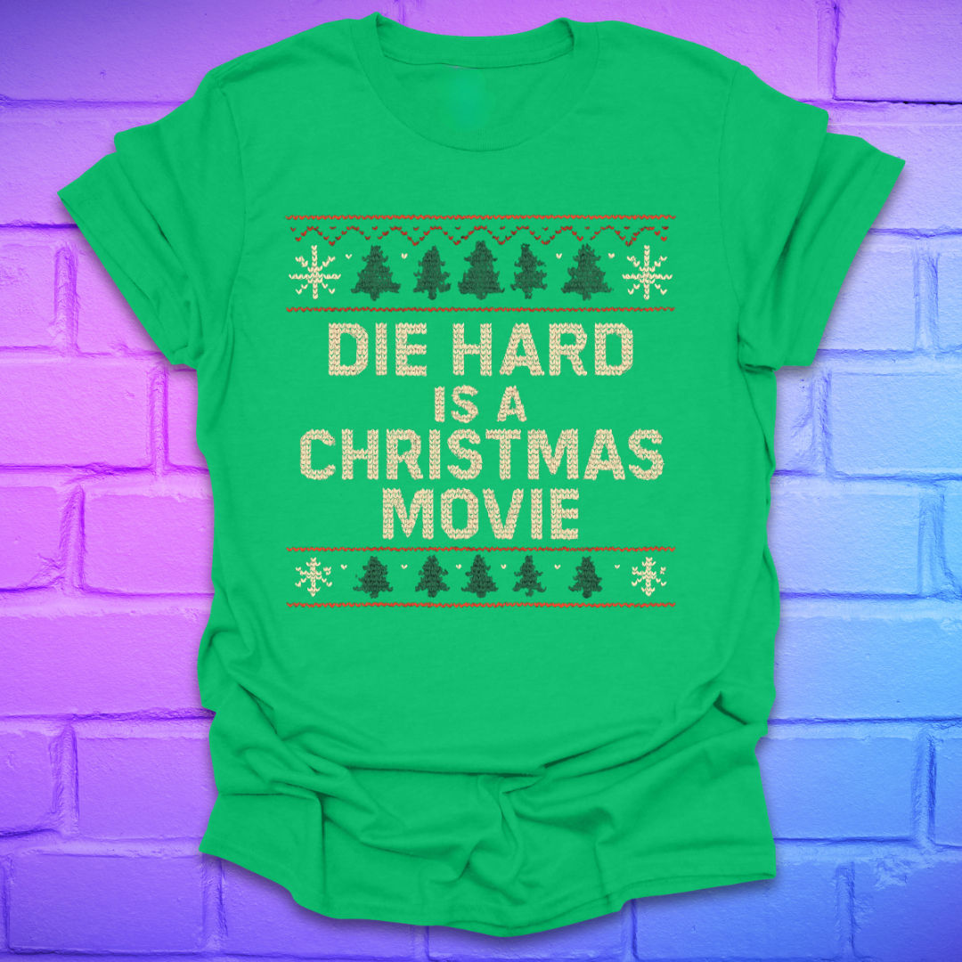 Green t-shirt with 'Die Hard is a Christmas Movie' text on a purple brick wall background