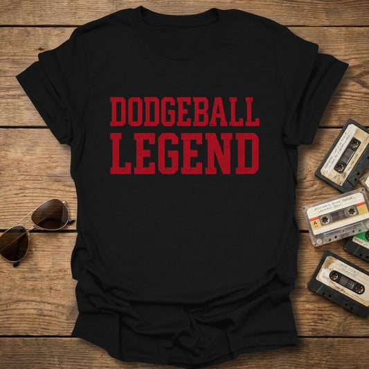 Black t-shirt with 'Dodgeball Legend' text on a wooden surface with sunglasses and cassettes.