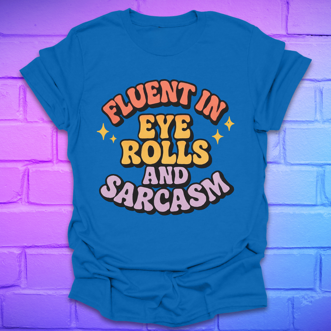 Royal blue t-shirt with colorful text, 'fluent in eye rolls and sarcasm' design on a purple brick wall background