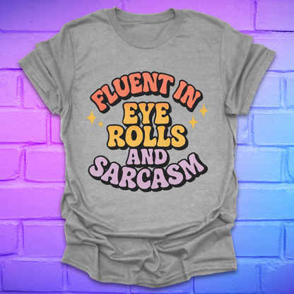 Grey t-shirt with colorful text, 'fluent in eye rolls and sarcasm' design on a purple brick wall background