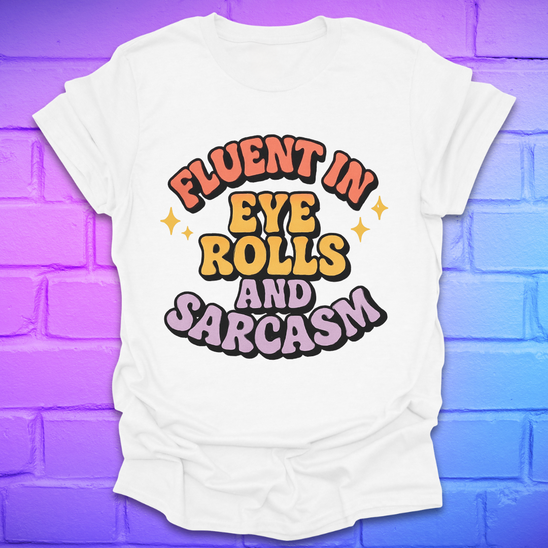 White t-shirt with colorful text, 'fluent in eye rolls and sarcasm' design on a purple brick wall background