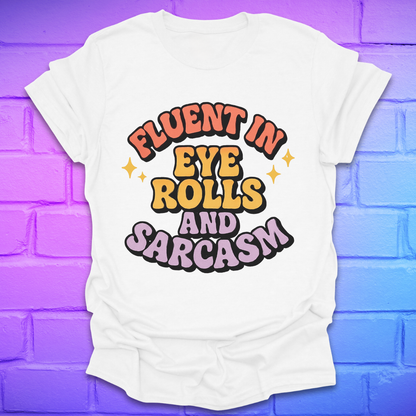 White t-shirt with colorful text, 'fluent in eye rolls and sarcasm' design on a purple brick wall background