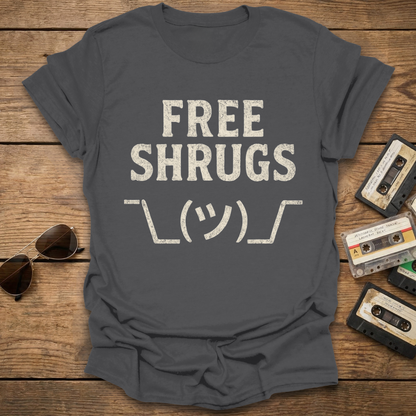 Gray t-shirt with 'FREE SHRUGS' text on a wooden surface with sunglasses and cassettes.
