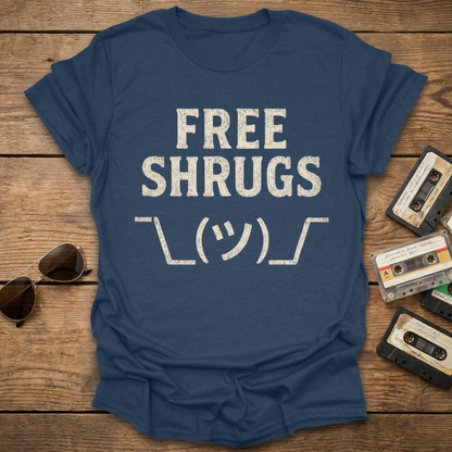 Blue t-shirt with 'FREE SHRUGS' text on a wooden surface with sunglasses and cassettes.