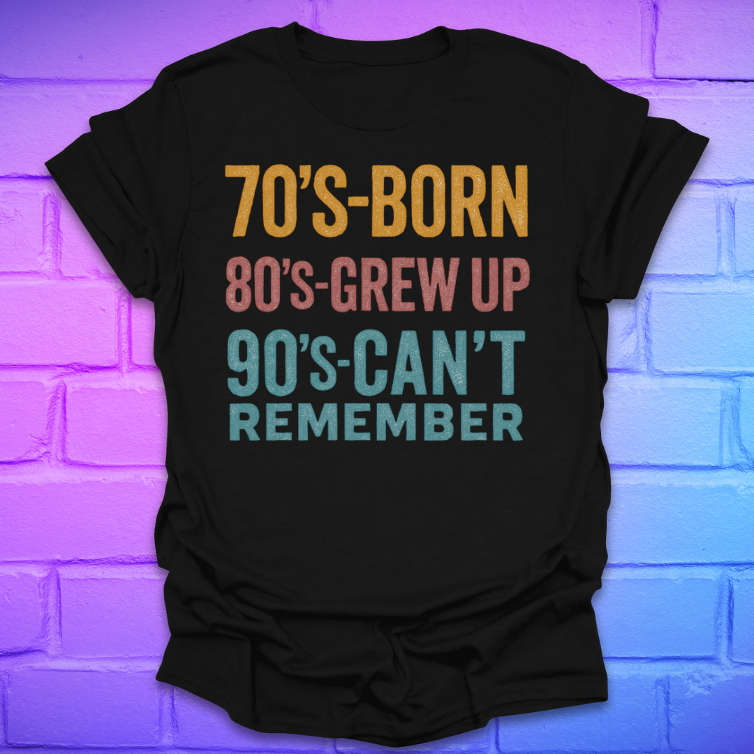 Black tshirt with colorful text '70's-born. 80's-grew up. 90's-can't remember' on a brick background.
