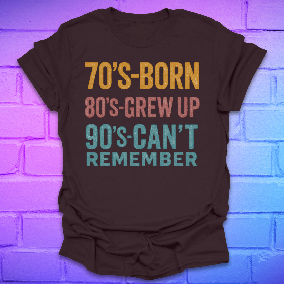 Brown tshirt with colorful text '70's-born. 80's-grew up. 90's-can't remember' on a brick background.