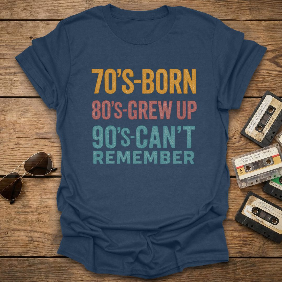 Blue t-shirt with '70's-born, 80's-grew up, 90's-can't remember' text on a wooden surface with cassette tapes and sunglasses.