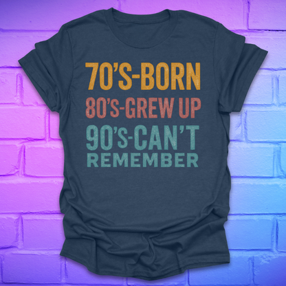 Heather navy tshirt with colorful text '70's-born. 80's-grew up. 90's-can't remember' on a brick background.