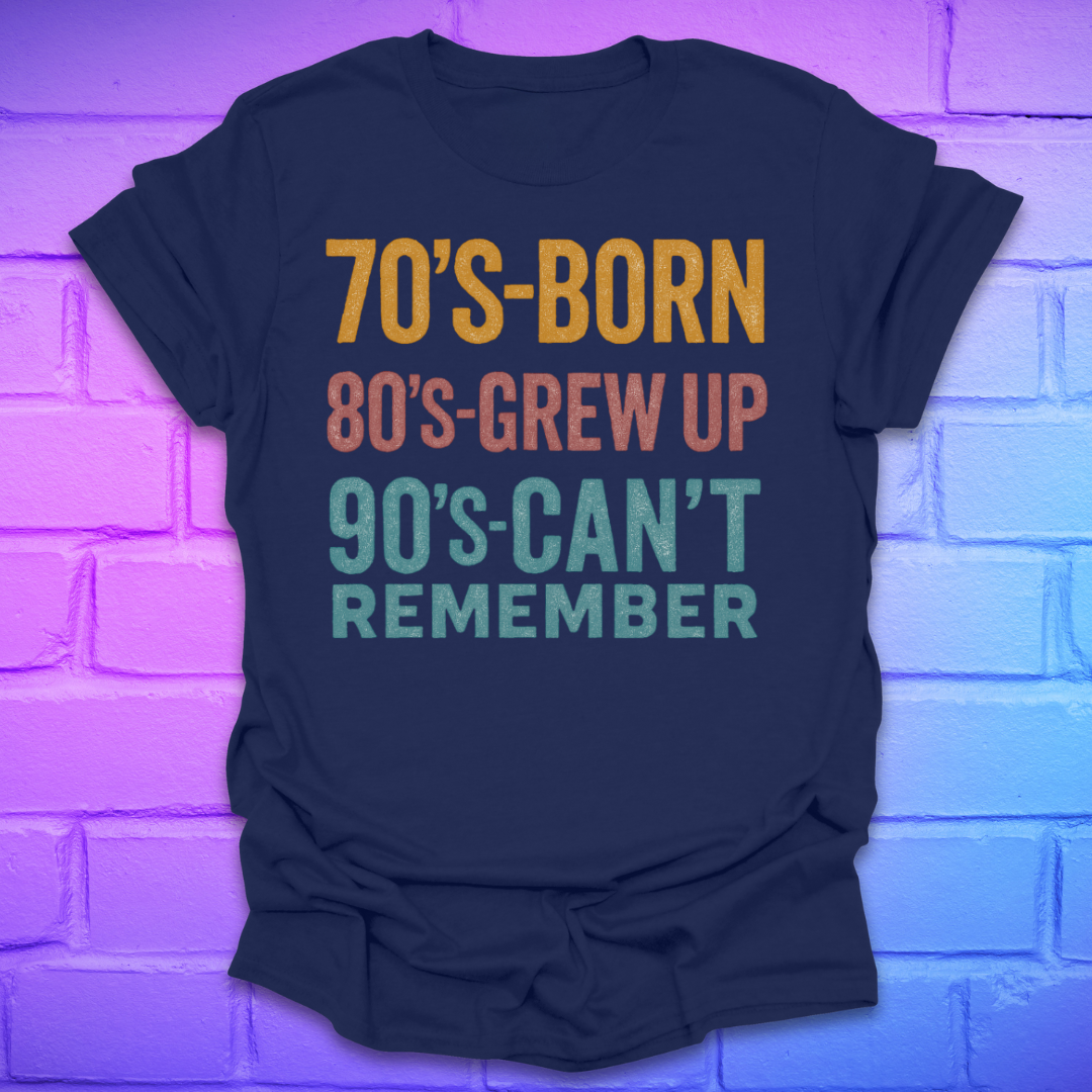 Navy blue tshirt with colorful text '70's-born. 80's-grew up. 90's-can't remember' on a brick background.