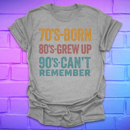 Grey  tshirt with colorful text '70's-born. 80's-grew up. 90's-can't remember' on a brick background.
