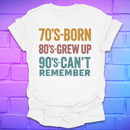 White tshirt with colorful text '70's-born. 80's-grew up. 90's-can't remember' on a brick background.