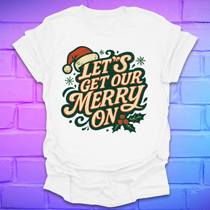 White t-shirt with Christmas-themed text, 'let's get our merry on' and graphics on a purple brick wall background