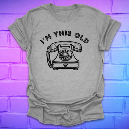 Gray t-shirt with a graphic of an old telephone and text 'I'm this old' on a brick wall background.