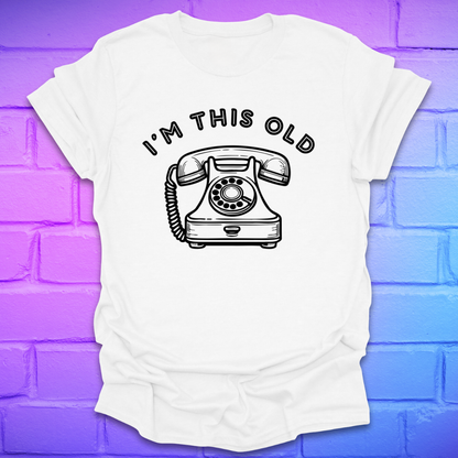White t-shirt with a vintage telephone graphic and text 'I'm this old' on a gradient purple to blue brick wall background.