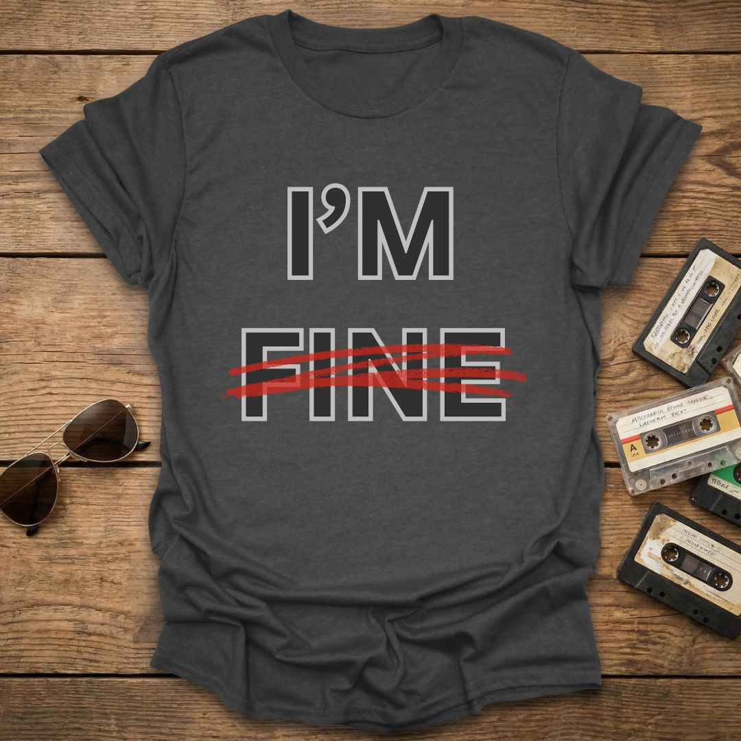 Dark grey t-shirt with 'I'm Fine' with fine crossed out in red text on a wooden surface with sunglasses and cassettes.
