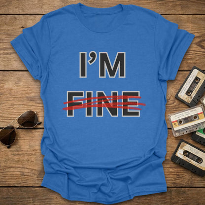 Royal blue t-shirt with 'I'm Fine' with fine crossed out in red text on a wooden surface with sunglasses and cassettes.