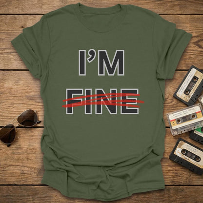 Green t-shirt with 'I'm Fine' with fine crossed out in red text on a wooden surface with sunglasses and cassettes.