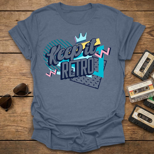 Blue t-shirt with 'Keep it Retro' design on a wooden surface with cassette tapes and sunglasses.