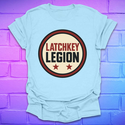 Light blue t-shirt with text, 'Latchkey Legion'  in a circle with stars design on a brick wall background