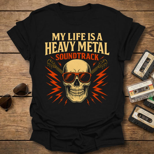 Black t-shirt with skull design and 'My Life is a Heavy Metal Soundtrack' text on a wooden surface with cassette tapes and sunglasses.