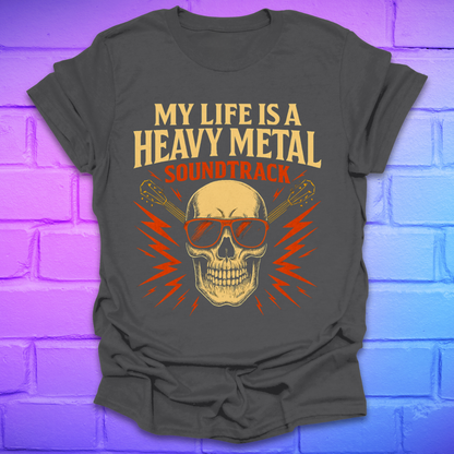 Charcoal colored t-shirt with a skull and guitar graphic and text, 'my life is a heavy metal soundtrack' on a brick background.