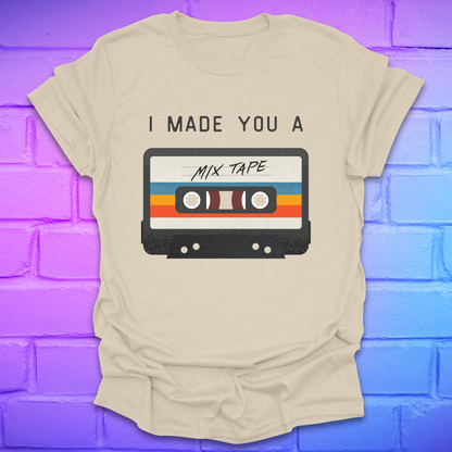 Beige tshirt with the text 'I made you a mix tape' with a graphic of a cassette tape on a brick background. 