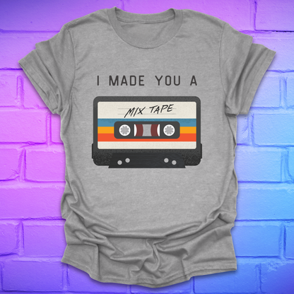 Grey tshirt with the text 'I made you a mix tape' with a graphic of a cassette tape on a brick background. 