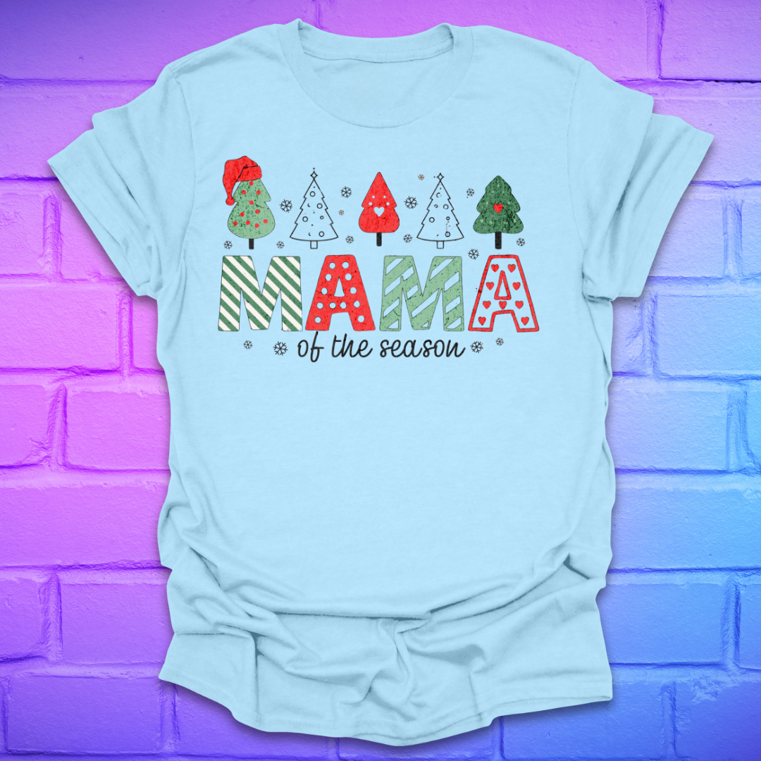 Light blue t-shirt with 'Mama of the season' text and Christmas tree graphics on a purple brick wall background.