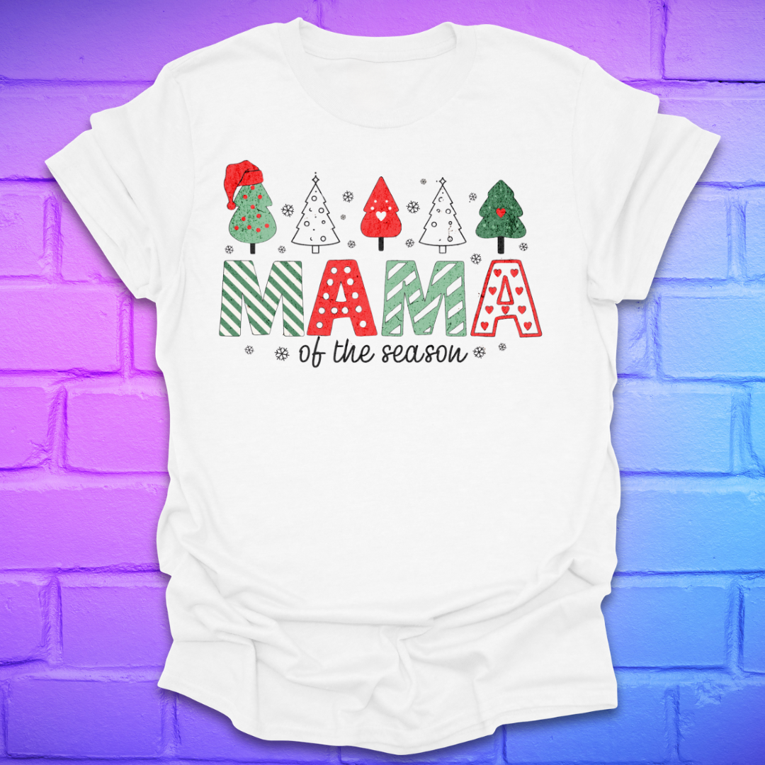 White t-shirt with Christmas-themed design and text, 'mama of the season' on a colorful brick wall background