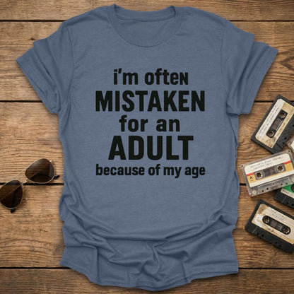 Blue t-shirt with humorous text on a wooden surface with sunglasses and cassettes.