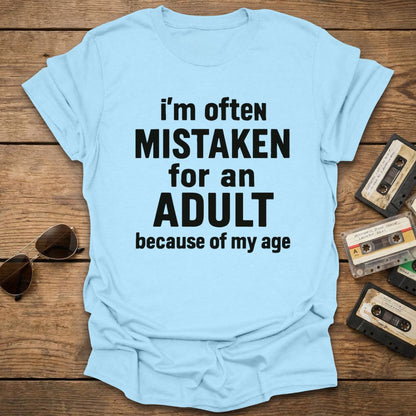 Light blue t-shirt with humorous text on a wooden surface with vintage items.