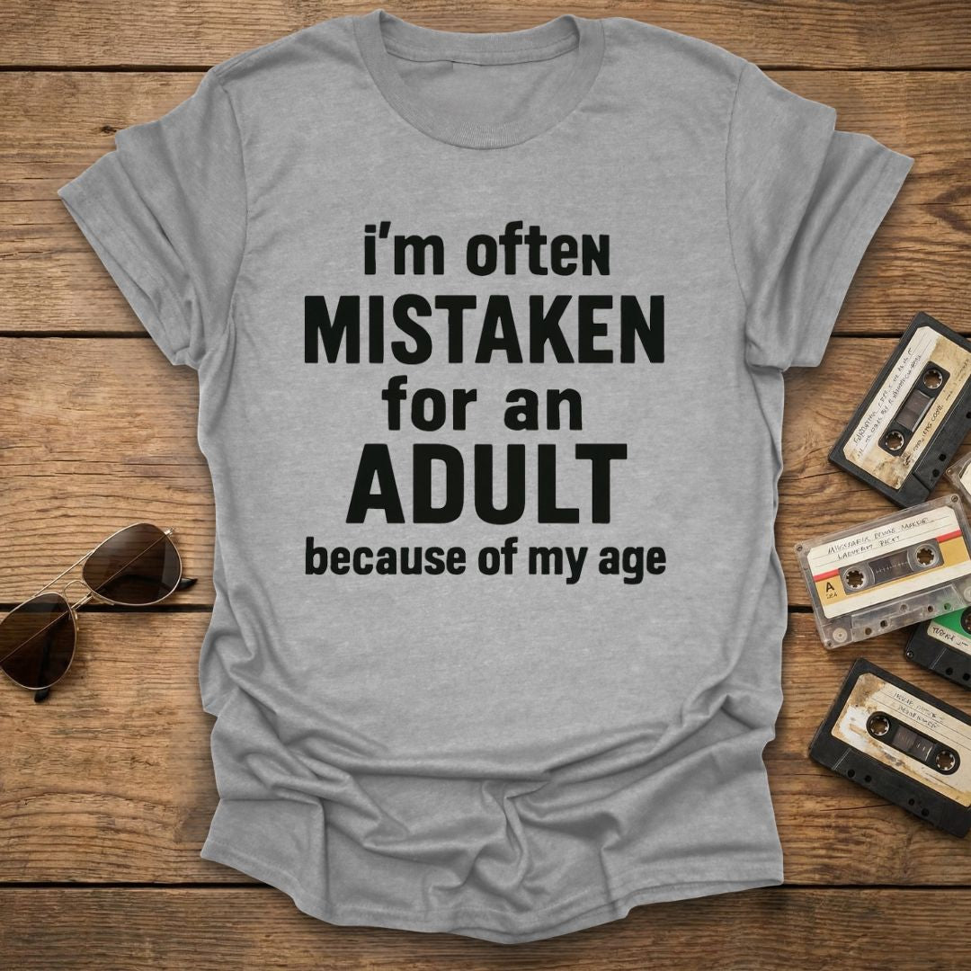 Gray t-shirt with humorous text on a wooden surface with vintage items.